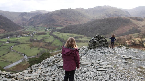 Two children look out from Castle Crag to the valley below on a cloudy spring day